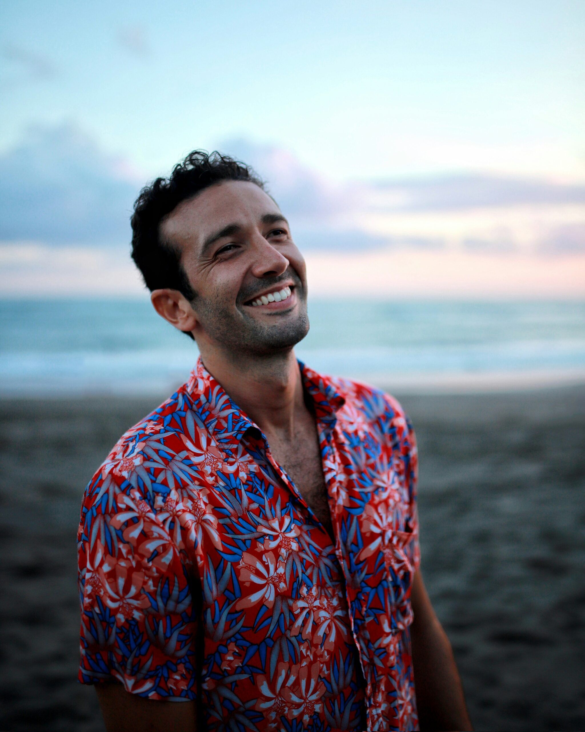 A man smiling on the beach at dusk, looking relaxed and present